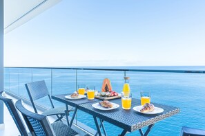 Ein Tisch mit Frühstücksangeboten und Getränken auf einem Balkon mit Blick aufs Meer.