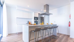 A modern kitchen with white cabinets, a central island with bar stools, and a stainless steel range hood. - Mar Apartment by Atlantic Holiday (Camara de Lobos)