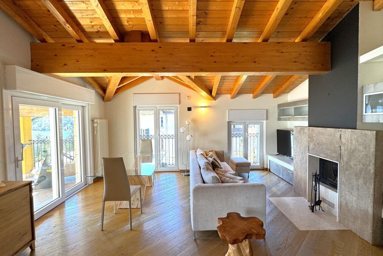 A spacious living room with wooden beams, a fireplace, and a large window.