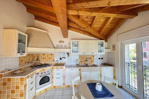A kitchen with white cabinets, a tiled backsplash, a gas stove, and a dining area with a table and chairs. - Ca Del Senior - Pool & Lake View (Azzano)