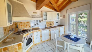 A kitchen with a gas stove, oven, white cabinets, and a dining area with a table and chairs. - Ca Del Senior - Pool & Lake View (Azzano)