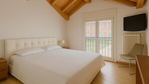A bedroom with a large bed, wooden ceiling beams, a TV, and a view of buildings through a glass door. - Ca Del Senior - Pool & Lake View (Azzano)