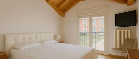A bedroom with a large bed, wooden ceiling beams, a TV, and a view of buildings through a glass door.