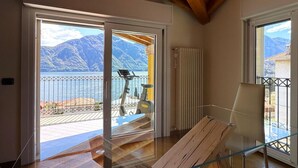 A room with a wooden ceiling, a glass table, and a view of mountains and water through open doors. - Ca Del Senior - Pool & Lake View (Azzano)