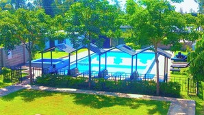 Una piscina con zona cubierta, rodeada de árboles y una valla.