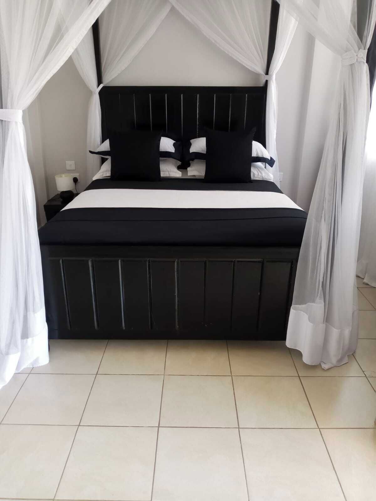 Una cama con estructura negra y ropa de cama blanca, rodeada de cortinas blancas.