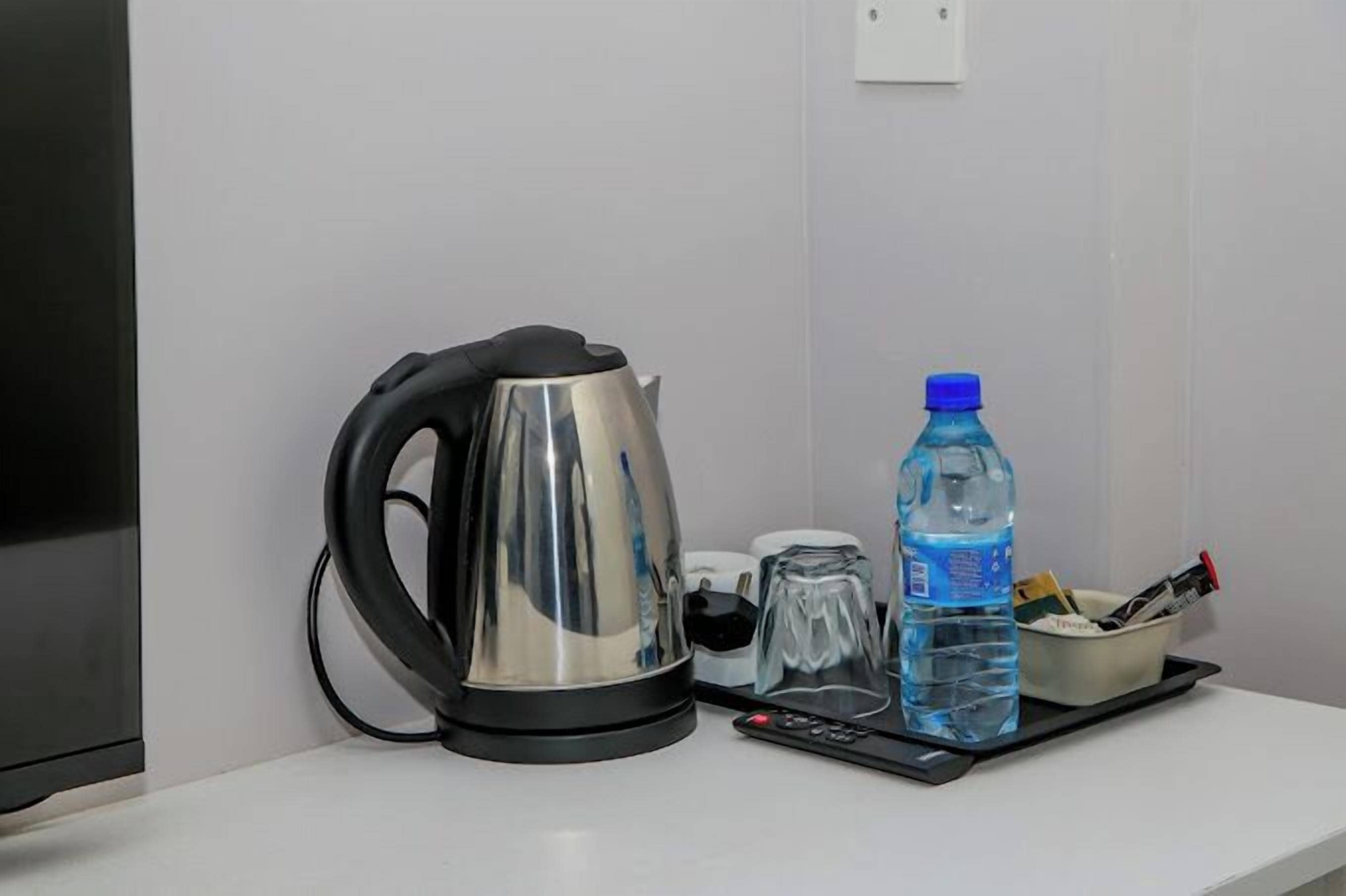 Una tetera, una botella de agua, un vaso y un control remoto sobre una mesa blanca.