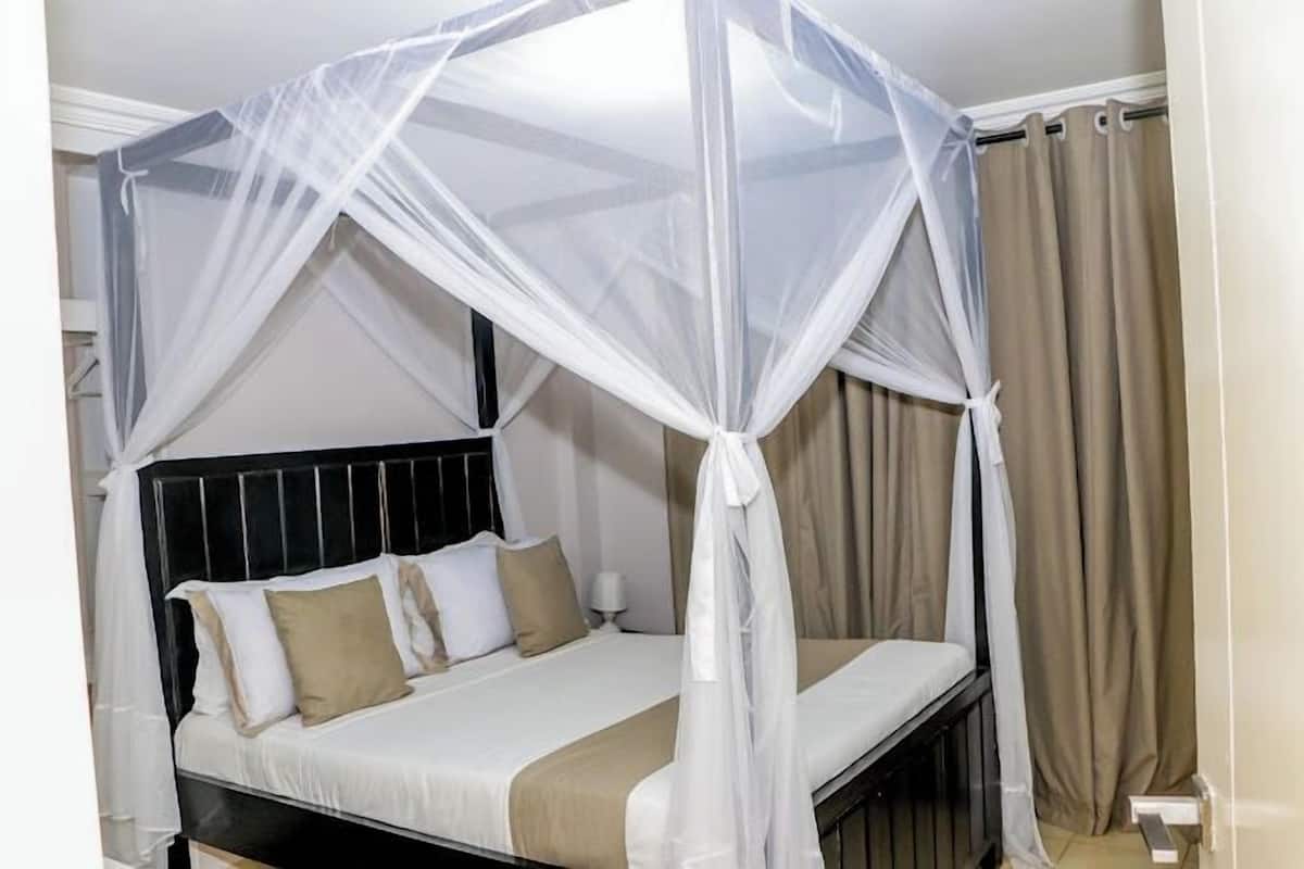 A bed with a white canopy, beige curtains, and a black headboard.