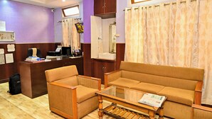 A hotel lobby with a reception desk, a sofa, a coffee table, and a television. - Holiday Inn Guest House (Guwahati)