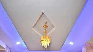 A room with a marble floor, wooden panel walls, a chandelier, and recessed ceiling lights. - Holiday Inn Guest House (Guwahati)