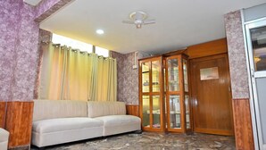 A room with a marble floor, a white sofa, a ceiling fan, and a wooden cabinet with glass doors. - Holiday Inn Guest House (Guwahati)