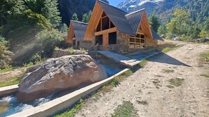 A rustic lodge with a stone foundation and wooden beams, set against a mountainous backdrop. - Shepherd's Lore Camps & Resort (Sangla)