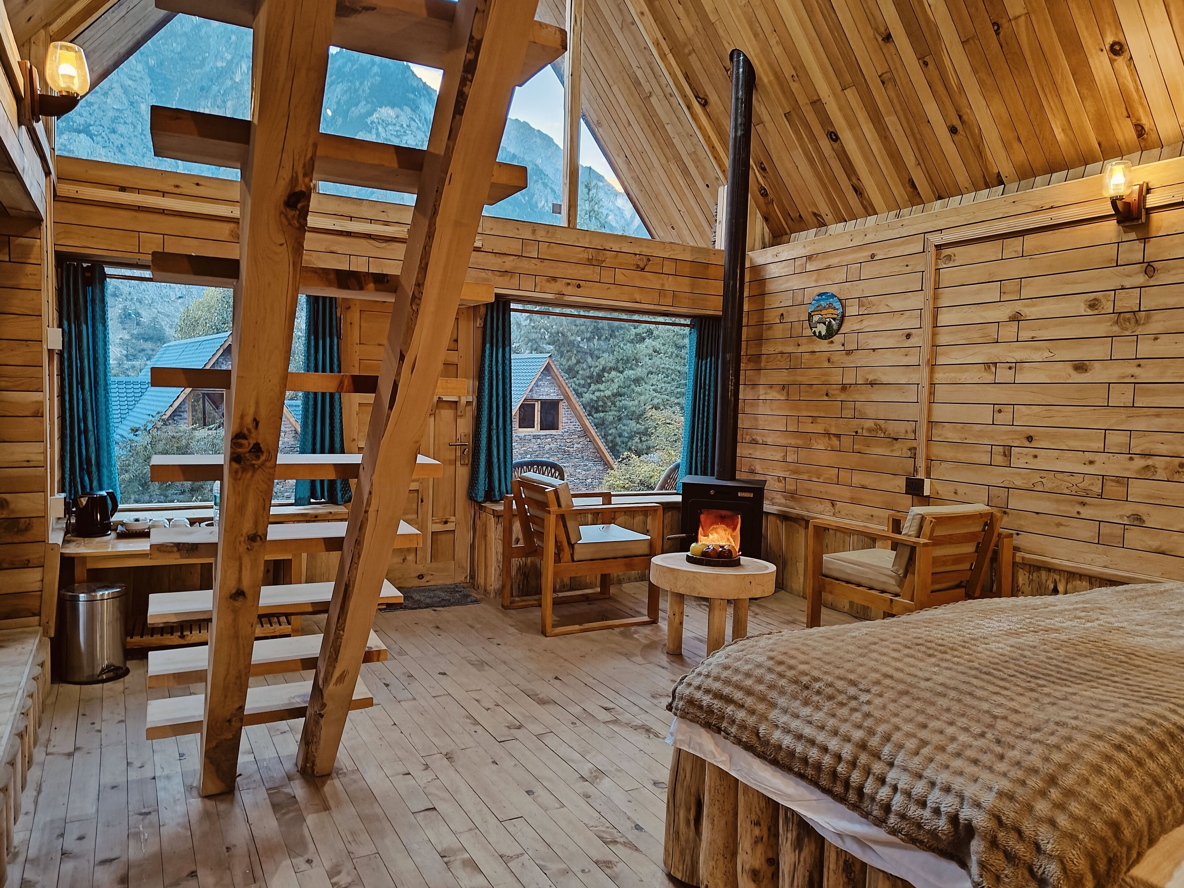 Ein gemütliches Blockhaus mit Holzwänden, einem zentralen Kamin und großen Fenstern mit Blick auf einen Berg.