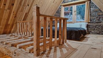 A wooden staircase leading to a loft bedroom with a stone wall and a window overlooking a snowy landscape.