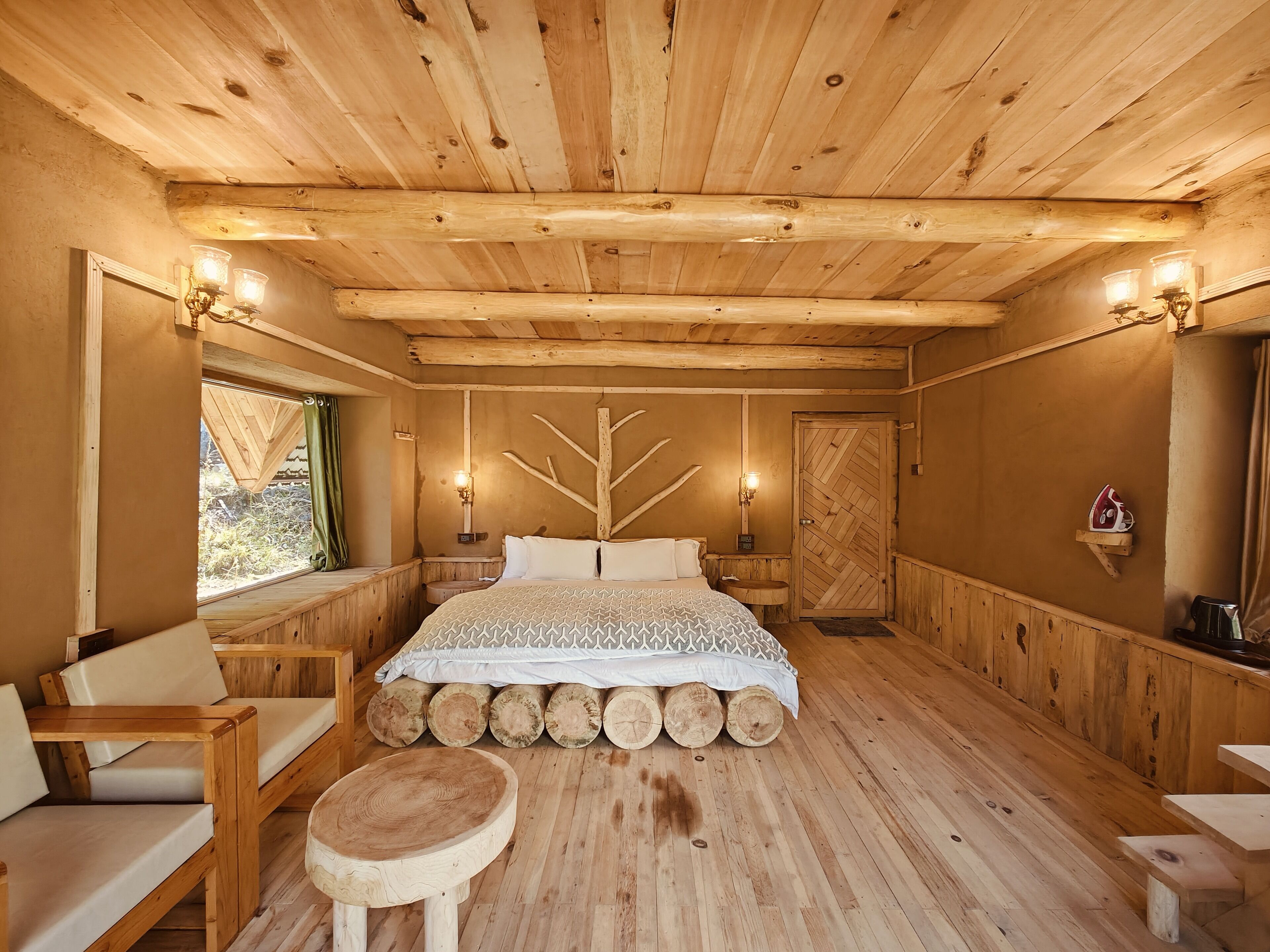 A wooden cabin bedroom with a bed, two bedside tables, a chair, a small stool, and a wooden wall decor.