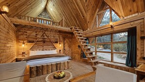 A wooden cabin interior with a bed, seating area, and a staircase leading to an upper level. - Shepherd's Lore Camps & Resort (Sangla)