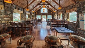A rustic dining area with stone walls, wooden beams, and hanging lanterns. Tables and chairs are arranged for dining. - Shepherd's Lore Camps & Resort (Sangla)