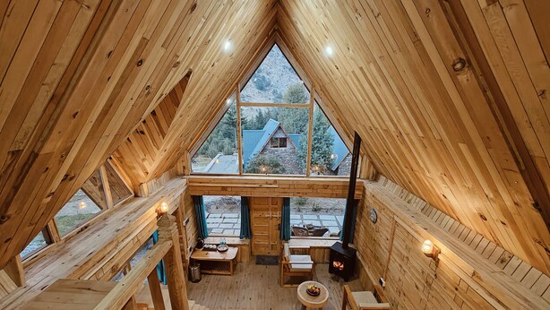 A wooden cabin with a sloped roof, a fireplace, and a view of a mountain landscape. - Shepherd's Lore Camps & Resort (Sangla)