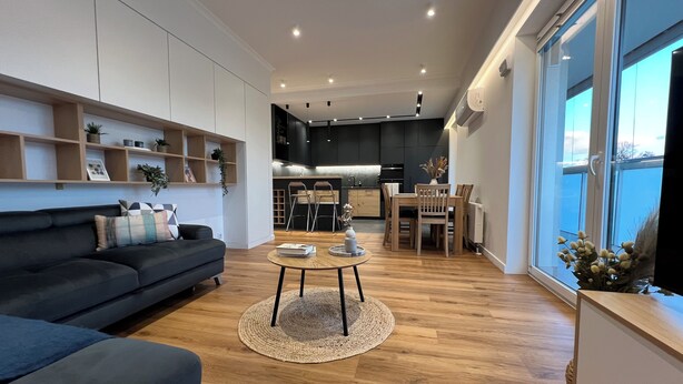 Ein modernes Wohnzimmer mit einem dunkelgrauen Sofa, einem Couchtisch und einem Essbereich mit Stühlen und Tisch.