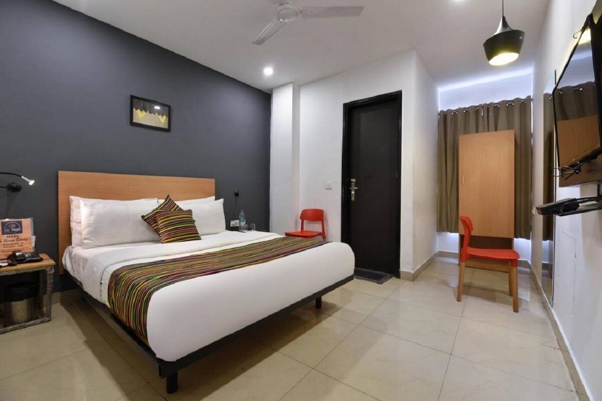Une chambre d’hôtel avec un lit, une table de chevet, une chaise, une porte et un ventilateur de plafond.
