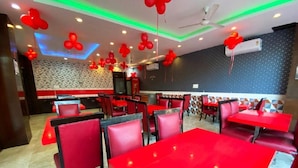 Ein Restaurantinnenraum mit roten Tischen und Stühlen, dekorativen roten Ballons und einer gemusterten Wand.