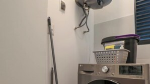 Ein Waschraum mit einer Waschmaschine mit Frontlader, einem Mop und einem Wandheizkörper.