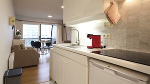 Una cocina compacta con armarios blancos, una cafetera roja y una ventana con vista a un paisaje urbano.