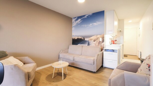 Una sala de estar con un sofá color beige, una mesita redonda y un armario blanco.
