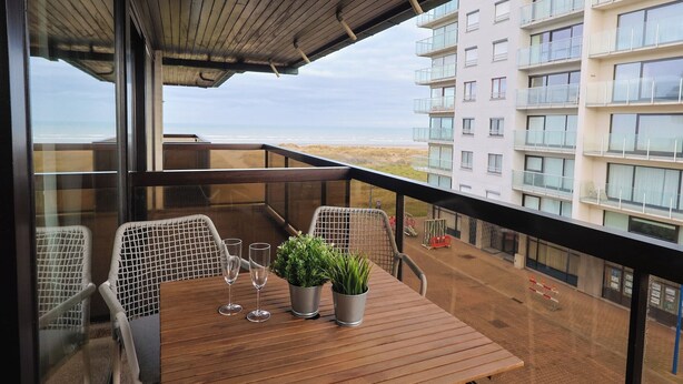 A balcony with a wooden table, two chairs, and potted plants.