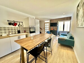 A modern kitchen with a wooden table and bar stools, a built-in oven, and a dining area with a blue sofa.