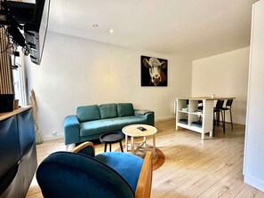 A modern living room with a green sofa, a blue armchair, a small round table, and a dining area with a white table and black chairs.