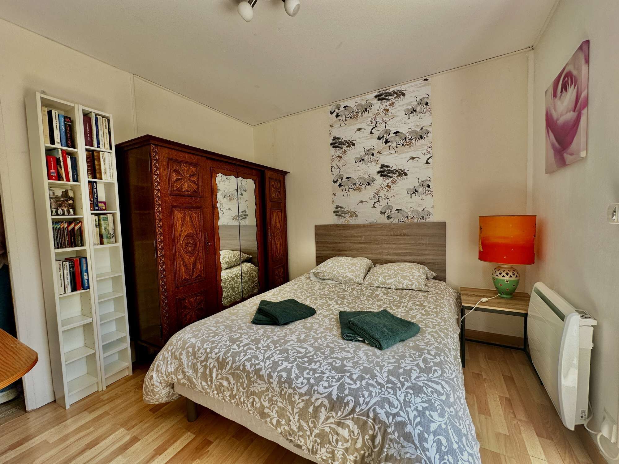 Une chambre à coucher comprenant un lit, une armoire, une bibliothèque, une tapisserie murale et un radiateur.