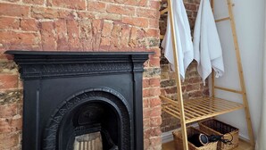 Une pièce avec une cheminée en briques, une étagère en bois en forme d’échelle sur laquelle sont posées des serviettes blanches, et des paniers en osier.