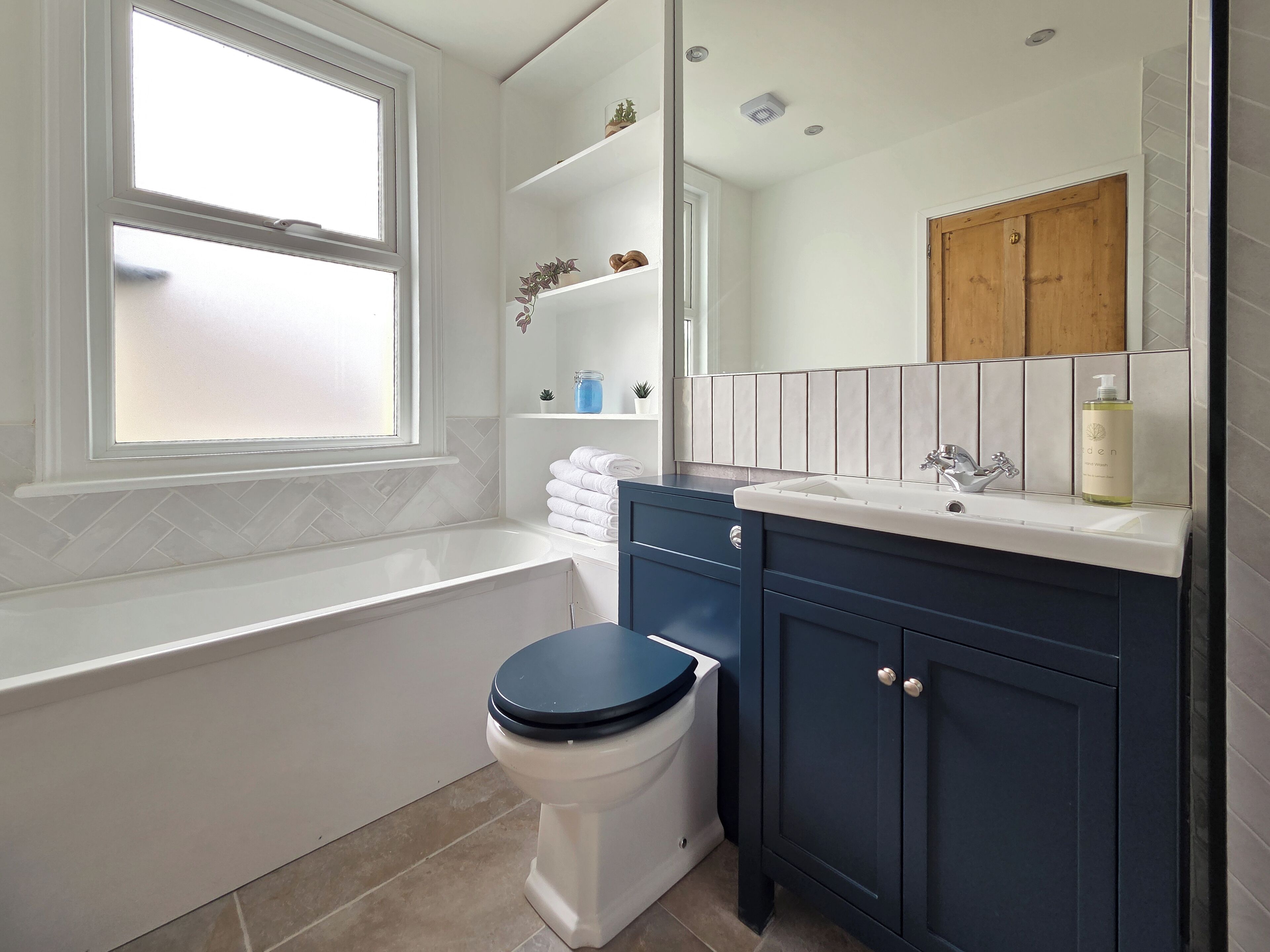 A bathroom with a white bathtub, a white toilet, and dark blue cabinets.
