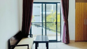 A room with a sofa, a small table, and a sliding glass door leading to a balcony. - LOUIS OTIS APARTMENT (Da Nang)