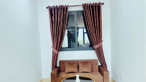 A room with a brown sofa, a glass coffee table with a gold frame, and brown curtains over a window. - LOUIS OTIS APARTMENT (Da Nang)