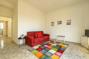 A room with a red sofa, a colorful rug, a small table with a plant, and a TV on a cabinet. - Operetta View Apartment (ROMA)