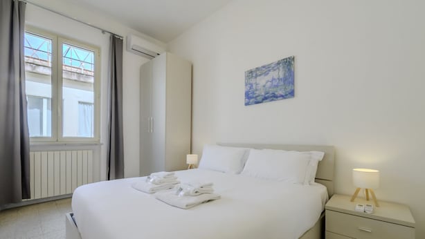 A hotel room with a bed, bedside table, lamp, and artwork on the wall. - Operetta View Apartment (ROMA)