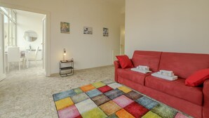 A living room with a red sofa, a colorful rug, and artwork on the wall. - Operetta View Apartment (ROMA)