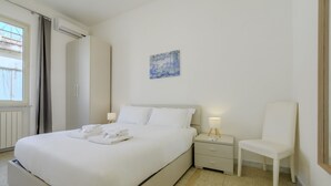 A hotel room with a bed, a chair, a nightstand, a painting, and a window. - Operetta View Apartment (ROMA)