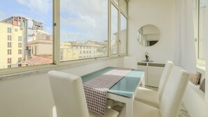 A room with a table, chairs, a round mirror, and a view of buildings through large windows. - Operetta View Apartment (ROMA)