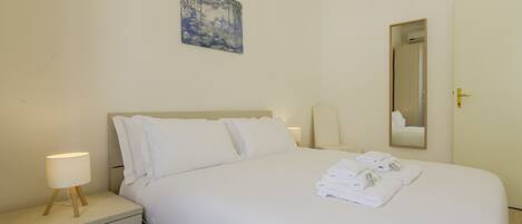 A hotel room with a bed, a nightstand with a lamp, a painting on the wall, and a mirror.