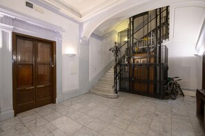 A grand hallway with a marble floor, a wooden double door, and a staircase with a metal railing. - Operetta View Apartment (ROMA)