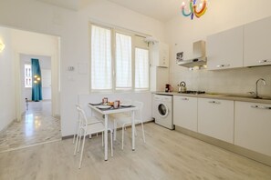 A modern kitchen with a washing machine, a dining area with chairs, and a window with curtains. - Operetta View Apartment (ROMA)