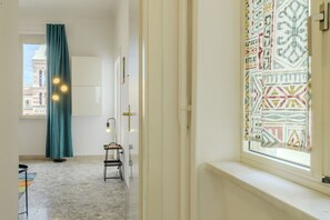 A room with a window, a chair, a floor lamp, and a patterned curtain. - Operetta View Apartment (ROMA)