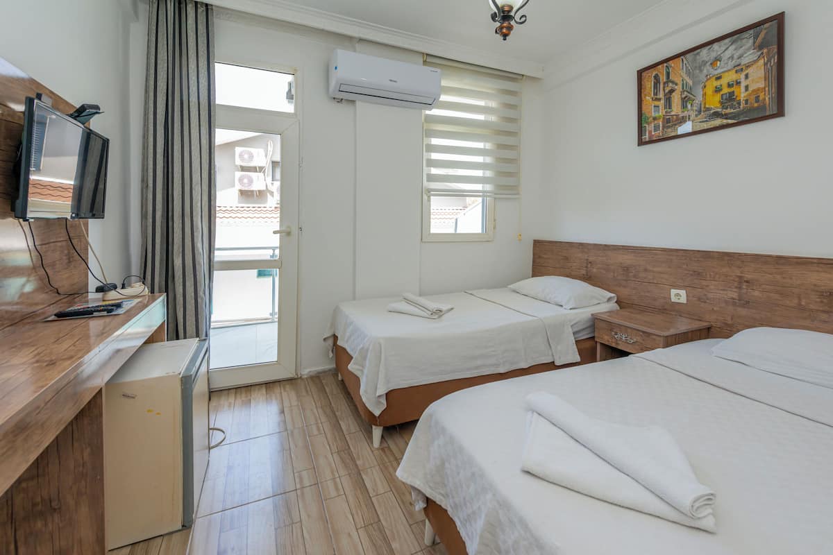 A hotel room with two beds, a desk with a television, an air conditioning unit, and a painting on the wall.