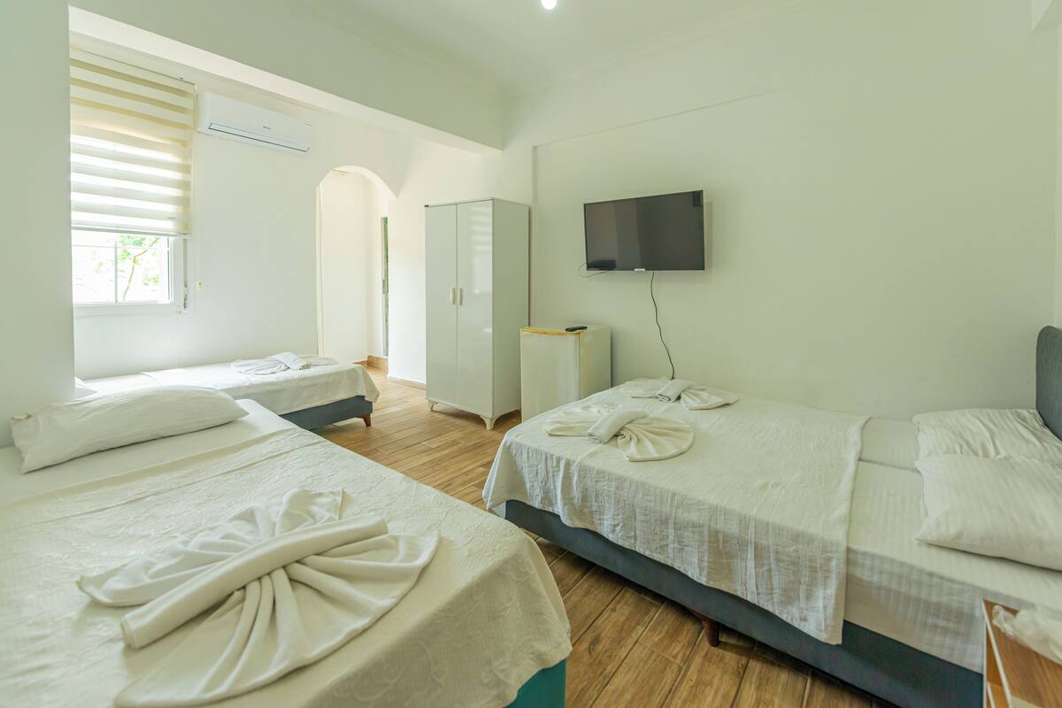 A hotel room with two beds, a TV, an air conditioner, and a window with blinds.