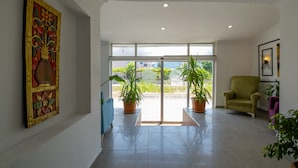 A spacious lobby with a large glass door leading outside, two potted plants, a blue sofa, a green armchair, and a framed artwork on the wall. - Aliş Hotel Fethiye (Fethiye)