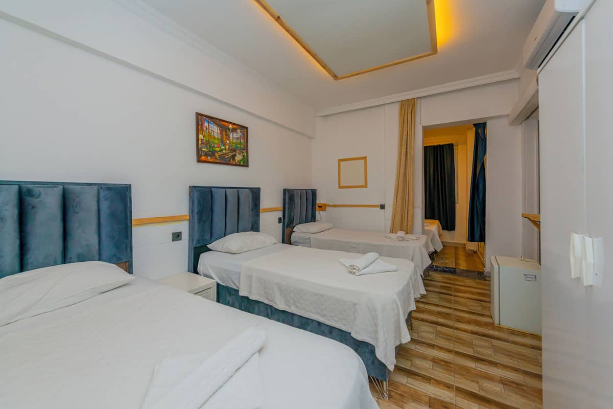 A hotel room with three beds, a painting on the wall, and a wooden floor.