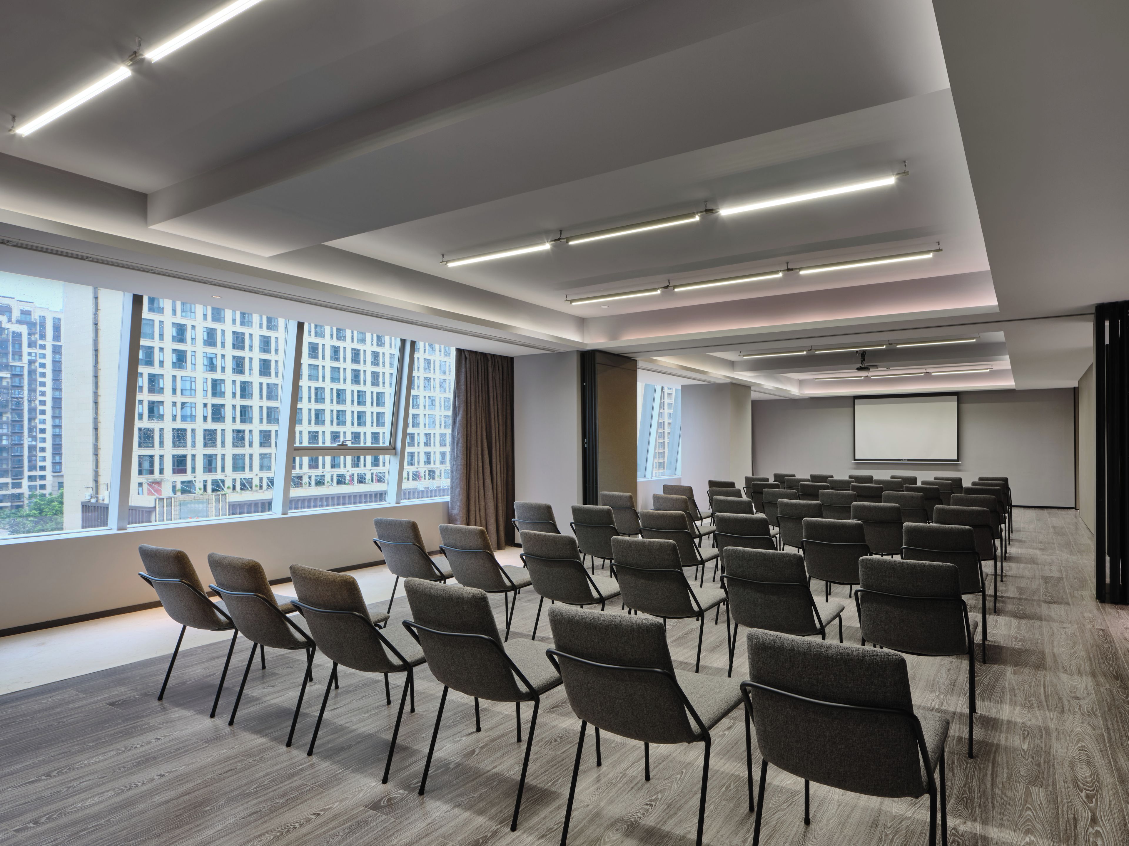 A conference room with rows of chairs, a projector screen, and large windows.